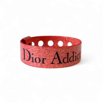 Dior pink color bracelet that glitters in light with the words Dior Addict stamped in black letters and multiple holes for size adjustment of button snap  closure